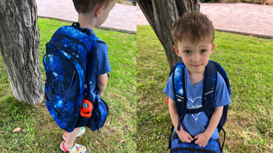 Small child wearing the Lands' End Kids ClassMate XL Backpack in the Blue Galaxy Space color pattern while holding blue lunchbox outdoors.