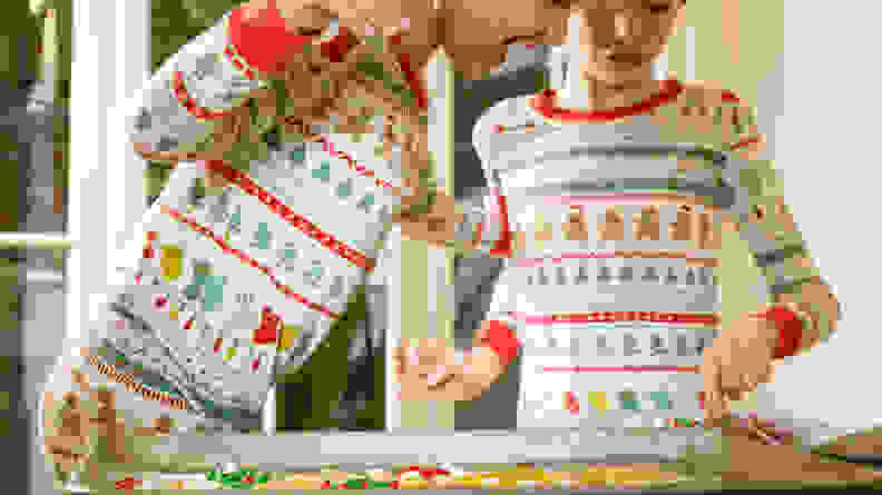 A boy and a girl wearing matching Christmas pajamas decorating cookies