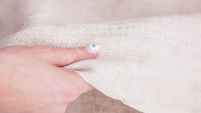 a hand holding a linen sheet up close with white stitching