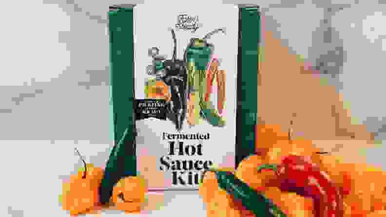 A Farm Steady hot sauce making kit sits on a marble surface surrounded by various citrus and peppers.