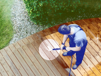 Person using power washer on wooden deck outdoors to clean boards.