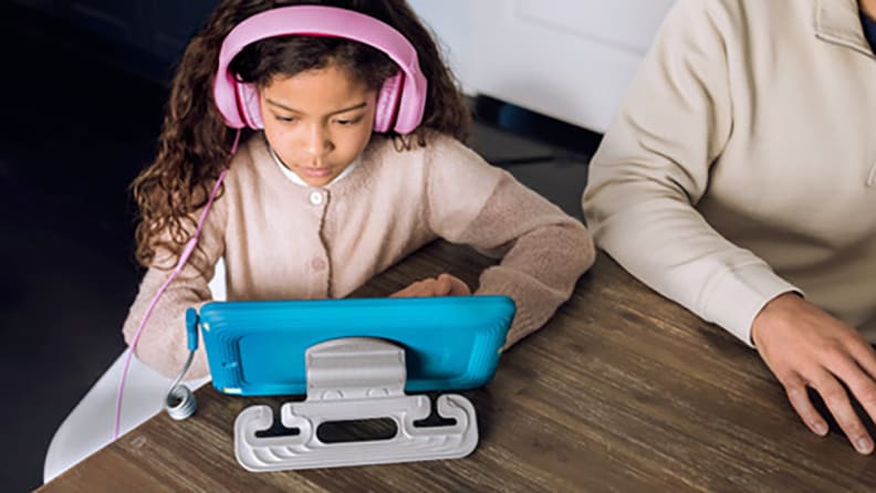 A young girl wearing headphones and looking at a tablet.