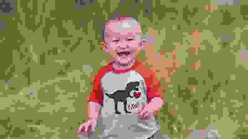 Child smiling wearing gray and red with dinosaur on front.