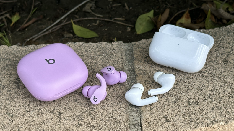 The Beats Fit Pro and Apple AirPods Pro 2 earbuds and cases on a stone wall.