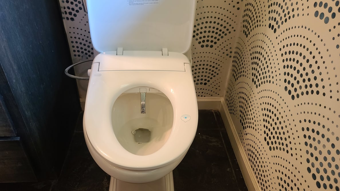 A toilet in a bathroom, with the Alpha Bidet UX Pearl installed on it.