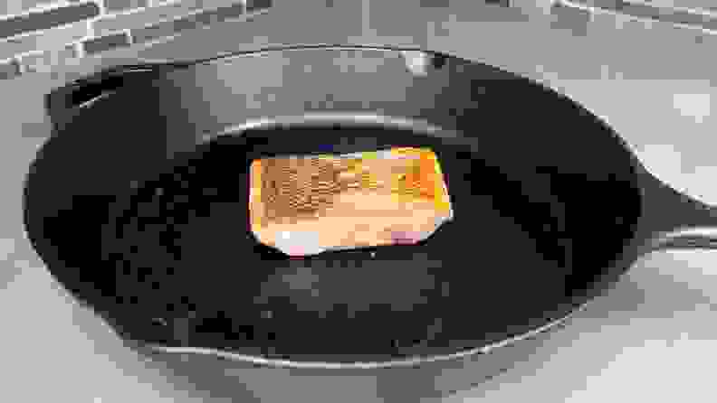 Small piece of salmon cooking in cast iron pan.