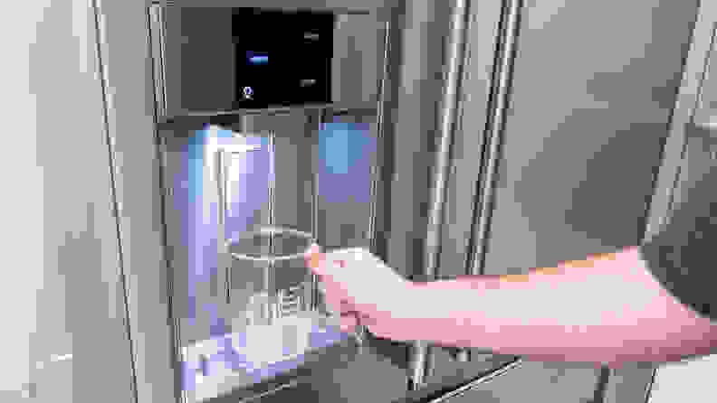 A hand reaches in with a large beaker, placing it against the paddle of an ice dispenser.