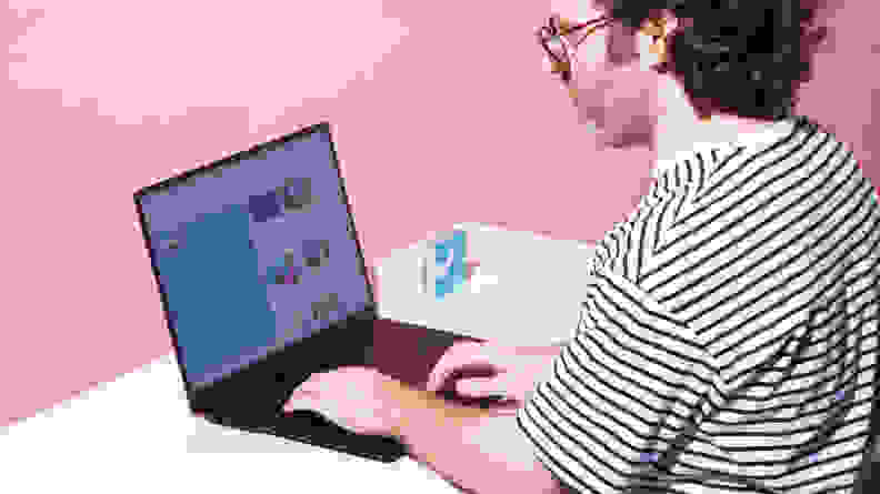 A man sitting in a chair, typing on the LG gram Pro 17 laptop on a white desktop with a pink background.