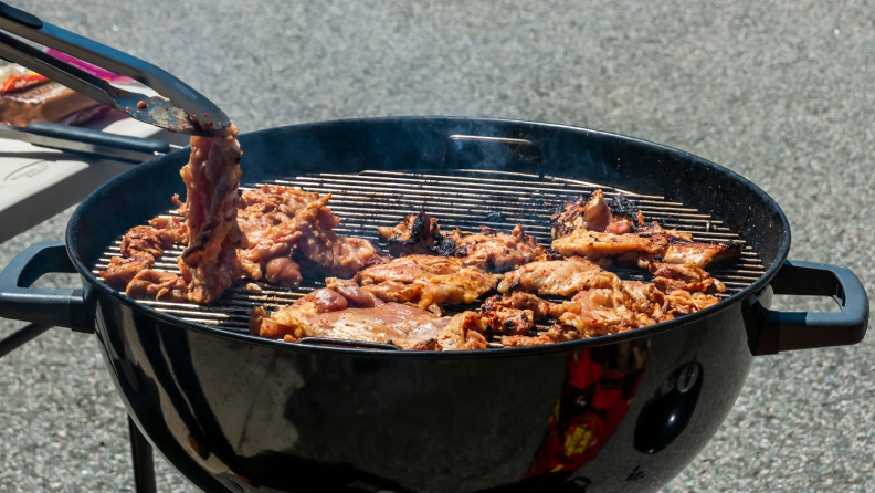 A pair of tongs turn chicken on a black grill.