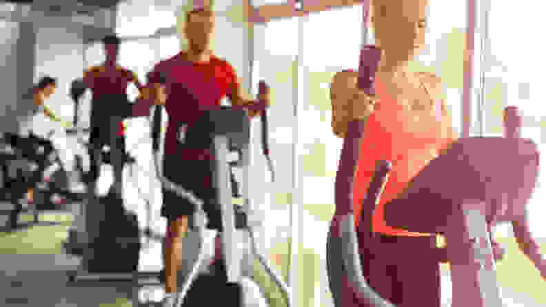 Three people using elliptical machines.