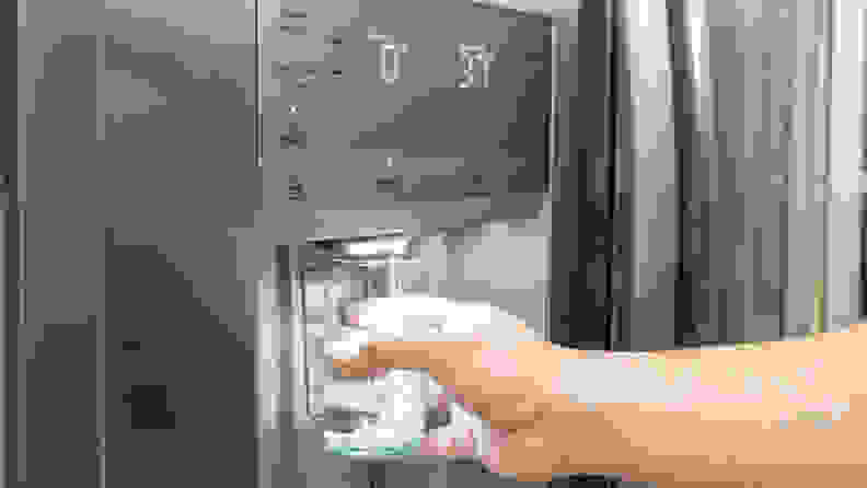 A hand reaches into frame, holding a glass against the water dispenser paddle on the front of the Frigidaire Gallery GRSC2352AF side-by-side refrigerator.