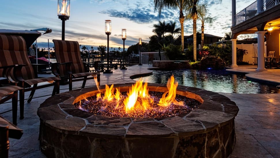 A fire pit lit up in a house's backyard next to a pool.