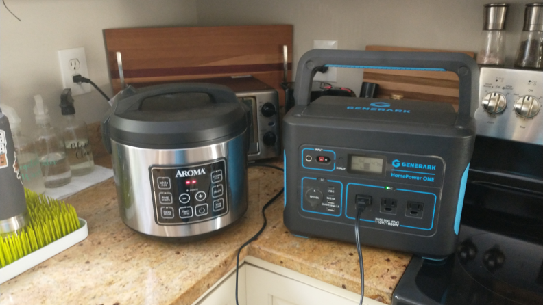 Small black and blue generator on countertop in kitchen powering a small pressure cooker.