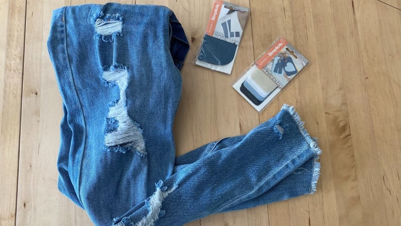 Distressed denim jeans on wooden floor next to patching packaging.