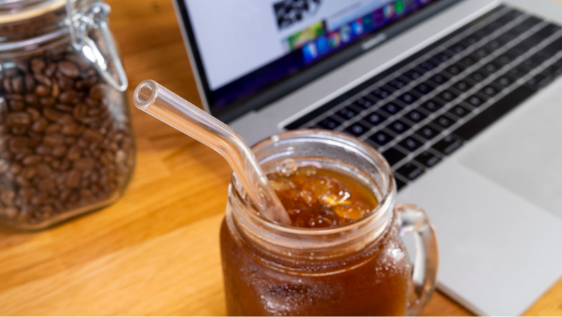 A glass straw is sticking out of a mason jar filled with cold drinks.