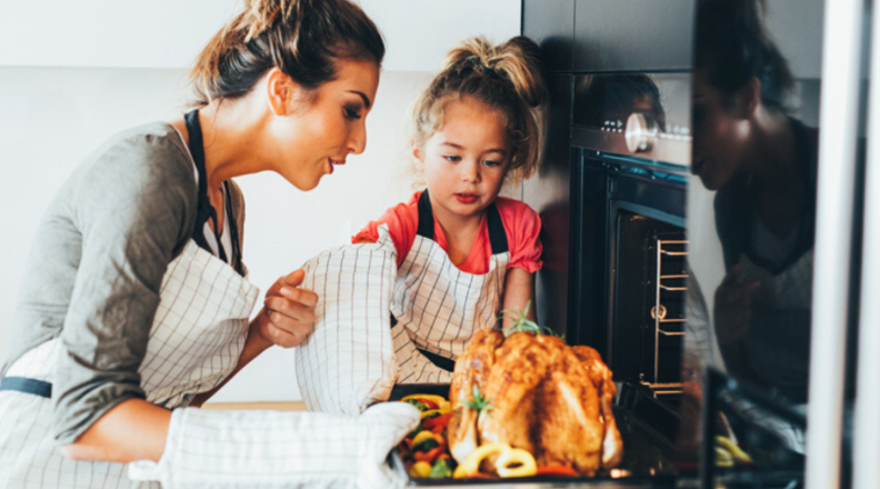 Woman and child checking on a turkey with the oven door open