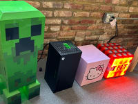 n array of novelty thermoelectric coolers set up to test in our office. They are, from left to right, a cooler in the shape of the Creeper enemy from Minecraft, an XBox, a small cube-shaped cooler with Hello Kitty's face on the front, and a cooler with the shape and design of a Minecraft TNT block.