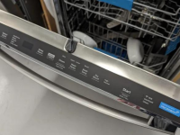 A stainless steel dishwasher door stands open and shows its top-facing control panel