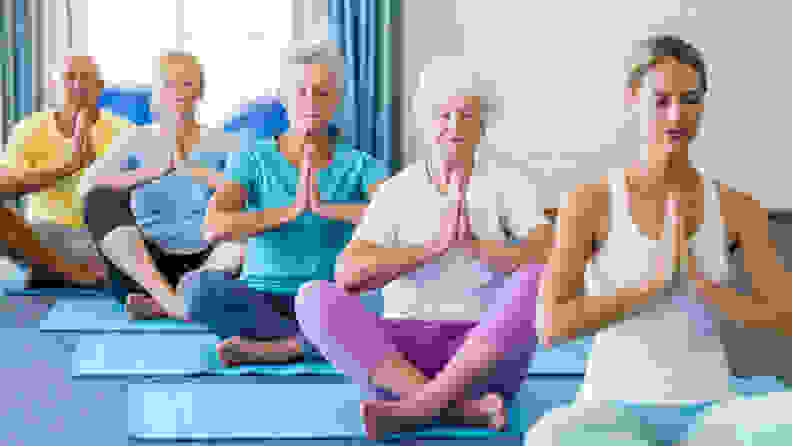 Led by an instructor, a group of seniors sits in a meditative pose on yoga mats