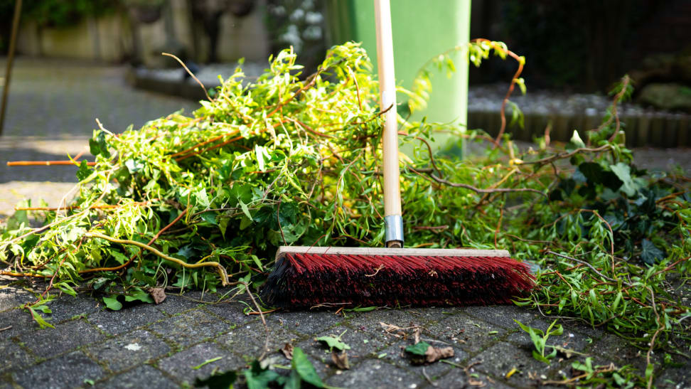 Large broom picking up branch and twig debris next to a green garbage can