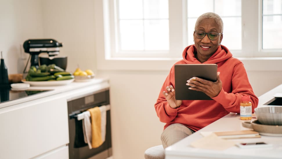 Senior woman smiling at tablet in well lit kitchen.