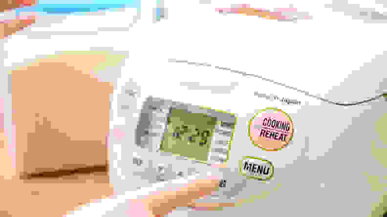 Hand pressing a button on a rice cooker.