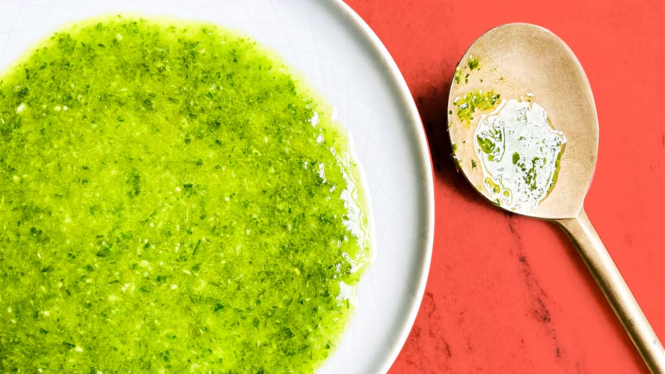 A small dish filled with herby green olive oil and a gold spoon next to it.