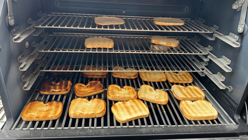 A batch of sliced white bread spread across the Masterbuilt grill interior, showing varying brownness