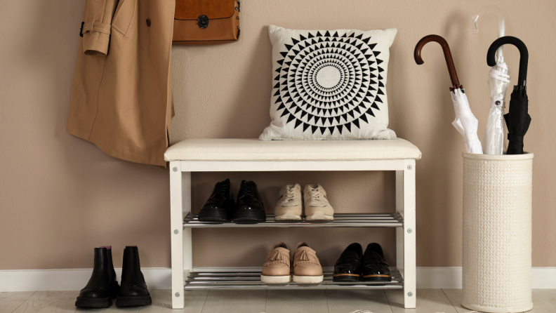 Shoe storage bench in home with shoes, clothing, and umbrellas.