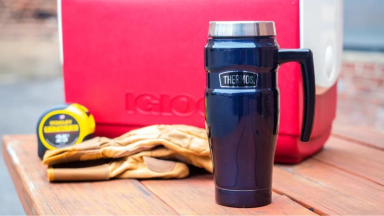 A Thermos travel mug sitting on a table next to a cooler.