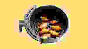 A batch of chicken wings in an air fryer basket, on a yellow background