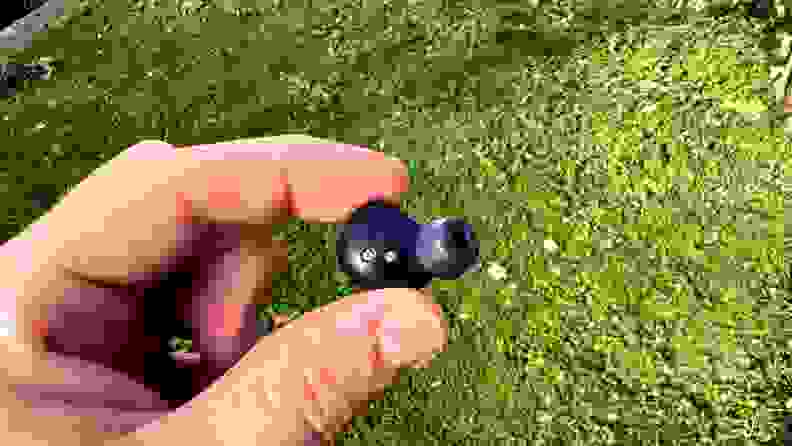 The interior of a navy earbud sits in a hand in front of a grassy backdrop.