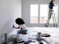 两个人准备粉刷卧室的墙壁;一个站在窗前的梯子上，一个跪在地上涂油漆布。