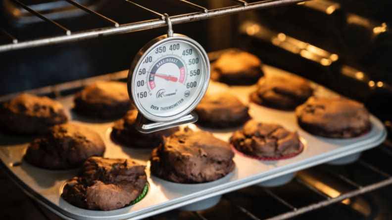 An oven thermometer hanging from a rack just above some chocolate cupcakes