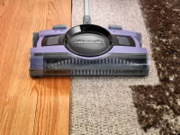 这是一张鲨鱼V2950无绳清扫机的特写照片，它是淡紫色的，正在清洁肮脏的地毯。