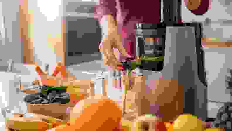 A hand working on pushing green juice out of a juicing machine, with fresh produce on the surrounding countertop.