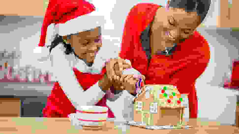 Adult and child wearing red in Santa hat decorating a gingerbread house