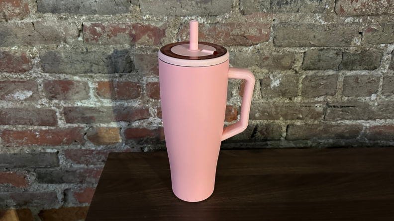 A pink 40 oz. tumbler sitting on a wooden table against a brick background.