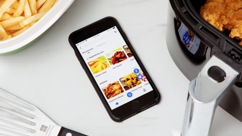 Smart phone with screen display on top of counter next to the Proscenic T22 Air Fryer filled with breaded chicken tenders and french fries.