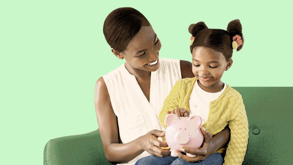 Small child sitting on child's lap while inserting money into pink porcelain piggy bank while sitting on couch.