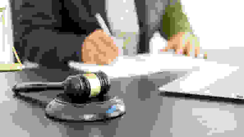 A hammer, a lawyer working on legal documents on a laptop and gold scale table.