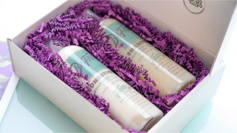 An image of Be Free shampoo and conditioner alongside each other in a box filled with purple confetti.