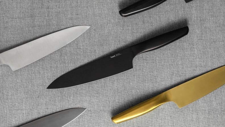 Three powder-steel Hast knives are on display, with the one in the center of the image being black, the one to the right gold, and the one to the left being silver.