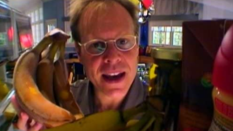 An image of Alton Brown peering into a fridge interior around a banana bunch.