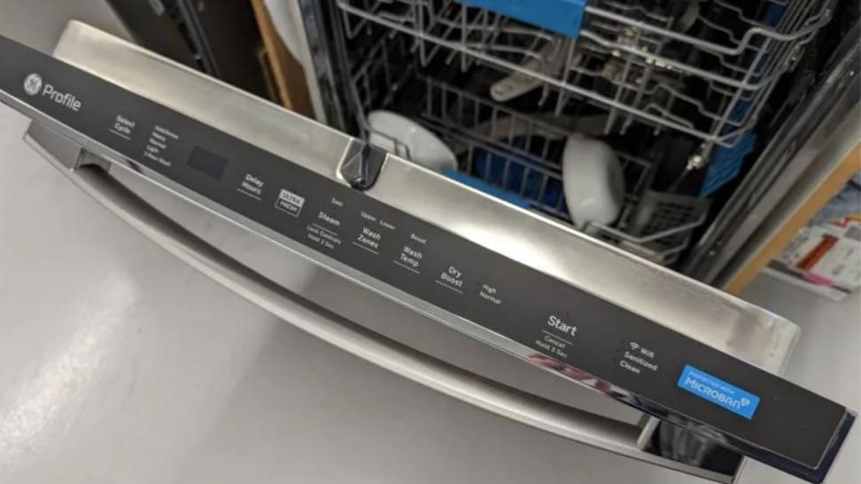 A stainless steel dishwasher door stands open and shows its top-facing control panel