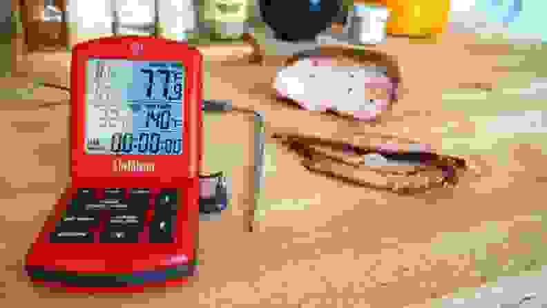 A probe thermometer sits on a kitchen counter next to freshly sliced brisket.