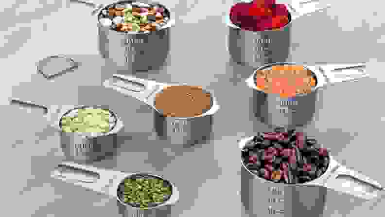 A set of stainless-steel measuring cups contains various seeds, berries, coffee beans, and so forth.