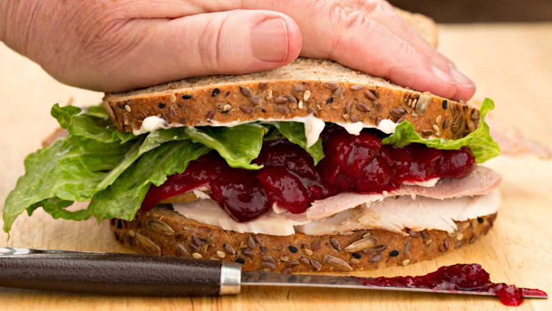 A hand pressing on a Thanksgiving leftover sandwich.