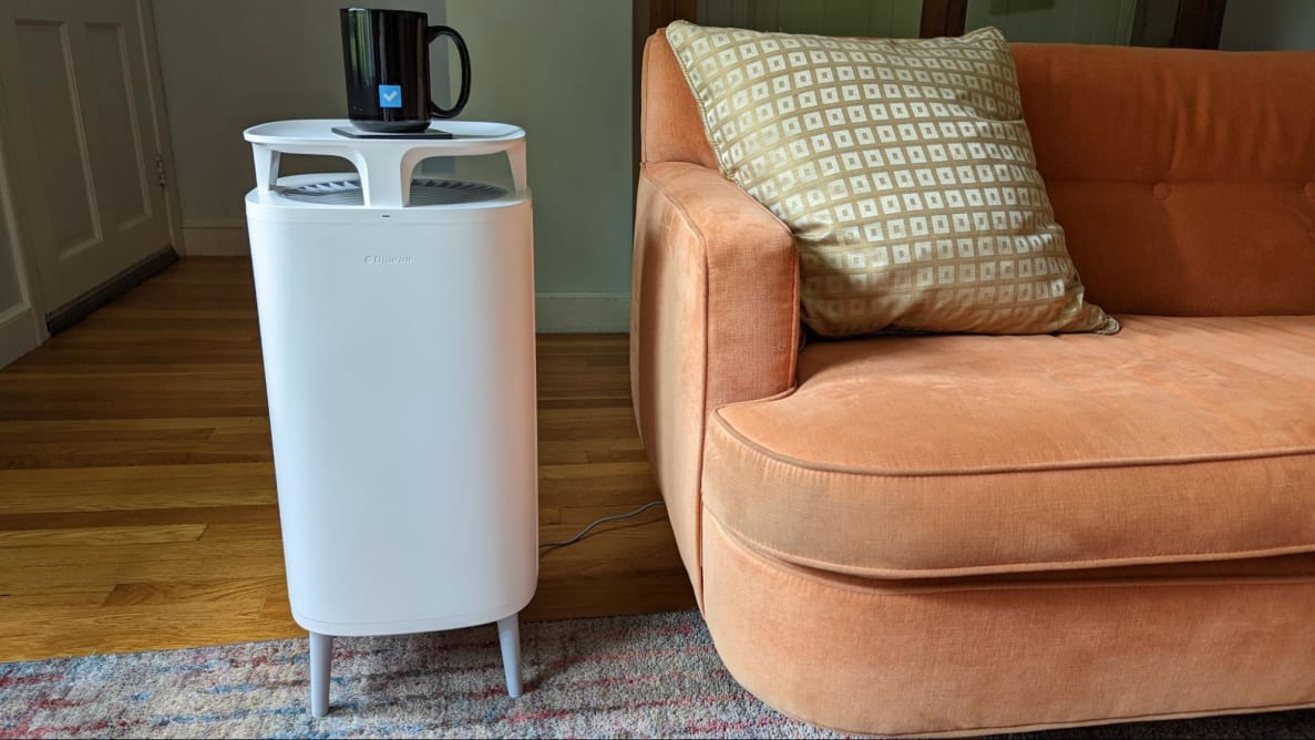 A standing air purifier placed in a living room next to a sofa.