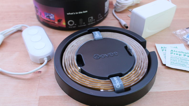 The Govee LED Strip Light inside of its original packaging next to assorted installation items on top of wooden surface.